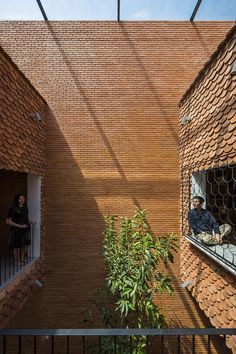 two people are sitting on the windowsills of an apartment building with brick walls