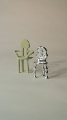 a small metal chair next to a little plastic chair on a white surface with a gray background