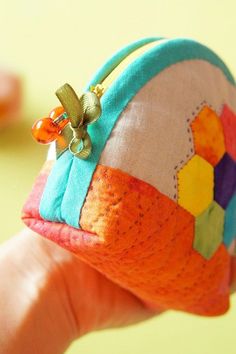 a hand holding an orange and blue patchwork coin purse with a flower on it