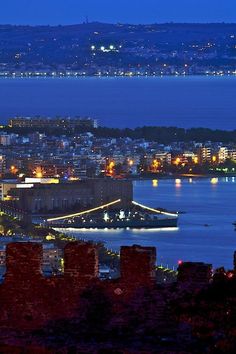 the city lights are lit up at night over the water and hills in the distance