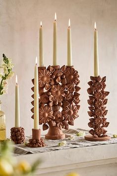 a table topped with lots of candles next to vases filled with flowers and leaves