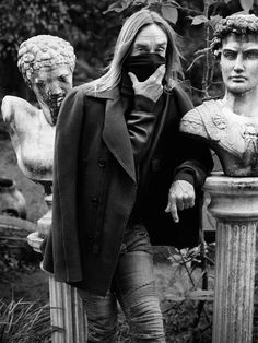 black and white photograph of woman with face mask standing next to statues in park area