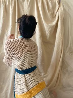 a woman standing in front of a white curtain wearing a crocheted sweater and skirt