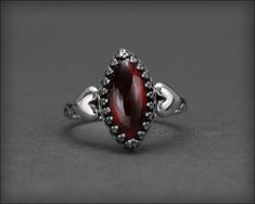 This gorgeous ring is uniquely beautiful and has a wonderful Victorian feel! A perfect gift for your sweetheart. The gemstone of your choice is set a gallery, bezel setting with two sterling silver hearts hugging each side. The ring has been oxidized to bring out all the lovely details. 𝙏𝙝𝙞𝙨 𝙙𝙚𝙨𝙞𝙜𝙣 𝙞𝙨 𝙤𝙧𝙞𝙜𝙞𝙣𝙖𝙡 𝙩𝙤 𝙇𝙀 𝙅𝙚𝙬𝙚𝙡𝙧𝙮 𝘿𝙚𝙨𝙞𝙜𝙣𝙨® 𝙃𝙖𝙣𝙙𝙘𝙧𝙖𝙛𝙩𝙚𝙙 𝙗𝙮 𝙇𝙖𝙪𝙧𝙚𝙣 𝙀𝙡𝙞𝙯𝙖𝙗𝙚𝙩𝙝. 𝙈𝙖𝙙𝙚 𝙞𝙣 𝙩𝙝𝙚 𝙐𝙎𝘼. • sold individually• made-to-order• s Elegant Sterling Silver Heart Ring For Promise, Marquise Sterling Silver Promise Rings, Elegant Accent Stones Jewelry For Valentine's Day, Oval Gemstone Heart Ring As Gift, Oval Gemstone Heart Ring For Gifts, Elegant Valentine's Day Jewelry With Accent Stones, Promise Jewelry With Marquise Accent Stones, Garnet Bezel Set Rings For Wedding, Garnet Jewelry With Bezel Setting For Wedding