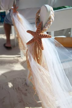 a starfish decoration hanging from the side of a white chair with tulle and feathers