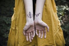 two hands holding each other with tattoos on their wrists and fingers in the shape of arrows