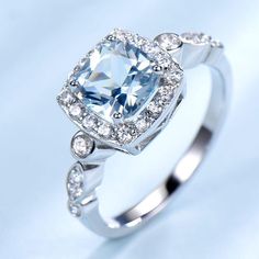 an engagement ring with a blue topazte surrounded by white diamonds on a light blue background