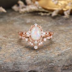 a white opal and diamond ring sitting on top of a rock