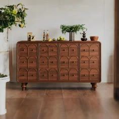 a wooden dresser sitting on top of a hard wood floor next to a potted plant