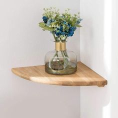 there is a vase with blue flowers in it on the corner of a wall shelf