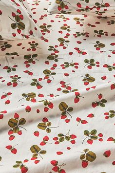 a white sheet with red cherries on it and green leaves in the center, sitting on a bed