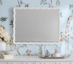 a mirror sitting on top of a white dresser next to a vase with flowers in it