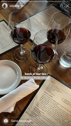 two glasses of wine sitting on top of a wooden table next to paper napkins