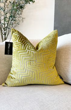 a yellow pillow sitting on top of a white couch next to a potted plant