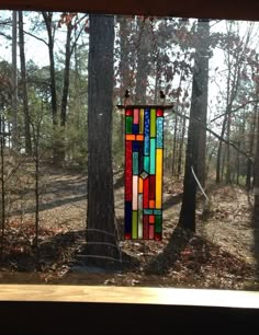 a multicolored stained glass wind chime hanging from a tree in the woods