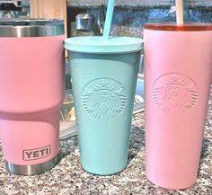 three different colored cups sitting on top of a counter next to each other and one has a straw in it