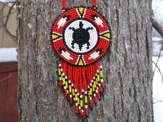 a red and yellow beaded necklace hanging on a tree trunk in the wintertime