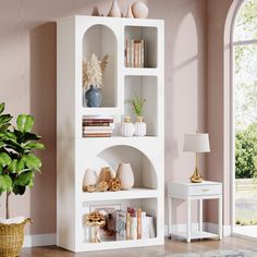 a white shelf with books and vases on it in front of a pink wall