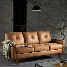 a tan leather couch sitting in a living room next to a coffee table and lamp