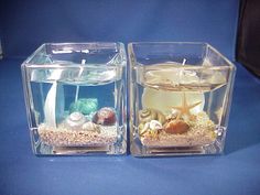 two clear cubes with candles and seashells in them on a blue surface