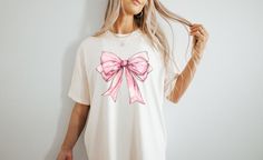 a woman wearing a white shirt with a pink bow on it