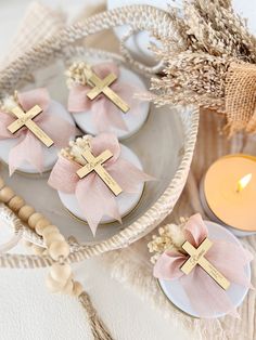 small cookies decorated with pink bows and gold crosses are on a plate next to a candle