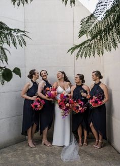 a group of women standing next to each other in front of a wall holding bouquets