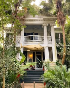 a white house surrounded by palm trees and greenery with stairs leading up to the front door