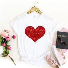 a t - shirt with a red heart on it next to some flowers and sunglasses