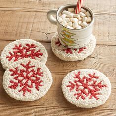 three crocheted coasters sitting on top of a wooden table next to a mug