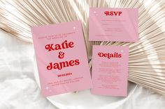 two pink wedding cards on a white plate next to some fanned bamboo sticks and a vase with flowers in it