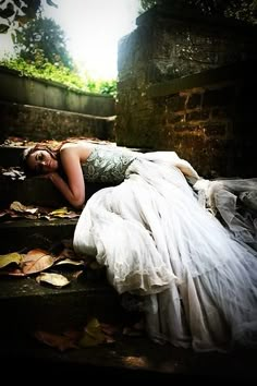 a woman in a white dress laying on some steps with her head down and eyes closed