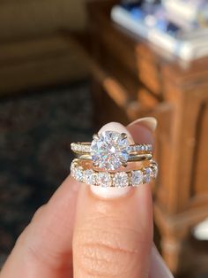 a woman's hand holding a diamond ring and two wedding bands on her finger