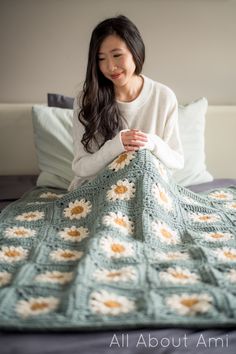 a woman sitting on top of a bed next to a green crocheted blanket