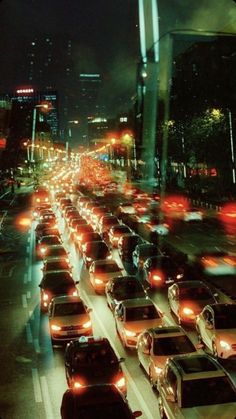 many cars are driving down the busy street at night, with city lights in the background