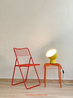 two orange chairs sitting next to each other in front of a wall with a lamp on it