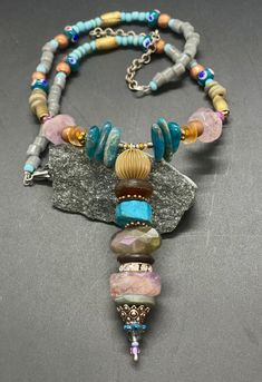 "Bohemian Longer gem necklace with a wired and beaded Pendant.  I just love colors, shapes, and different sizes in materials.  You will see apatite stone, lavender amethyst, vintage glass, wood, brass, copper, wood, lamp work beads hand crafted from Thailand and glass tube beads from Africa, in this unique necklace.  I wired the pendant and stacked up the beads.  I crafted the curved portion of this necklace and beaded onto wire; this helps to hold the curved shape.  Then I beaded strands from t Bohemian Beaded Necklaces With Round Stones, Bohemian Beaded Necklaces For Healing, Bohemian Long Beaded Necklaces With Stones, Bohemian Long Beaded Stone Necklace, Bohemian Healing Stone Necklaces, Bohemian Beaded Gemstone Dangle Necklace, Bohemian Beaded Gemstone Dangle Necklaces, Bohemian Dangle Crystal Necklace With Gemstone Beads, Bohemian Dangle Gemstone Beaded Necklaces