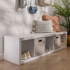 a white bench with several storage bins and shoes hanging on the wall next to it