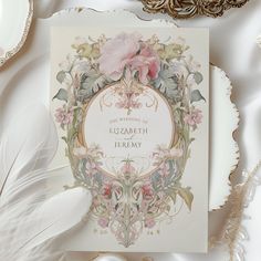 a wedding card with a pink flower on it next to some feathers and other items