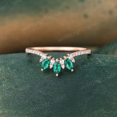 an emerald and diamond three stone ring on top of a green piece of wood in front of a plant