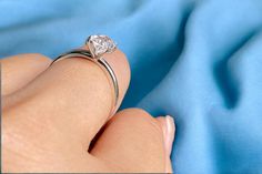 a woman's hand with a diamond ring on top of her finger in front of a blue cloth