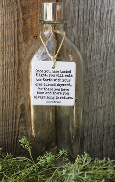 an empty glass bottle with a poem on it sitting next to some green plants and wood