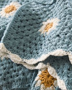 a crocheted blanket is laying on top of a bed with yellow and white flowers