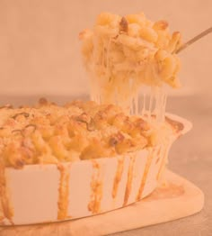 a person scooping macaroni and cheese out of a casserole dish