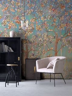 a room with a chair, bookcase and wallpaper that has a tree on it