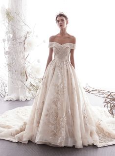 a woman in a wedding dress is standing on a white carpet with flowers and branches