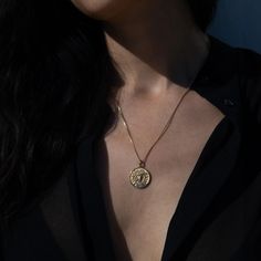 a woman wearing a black shirt and a necklace with a gold disc pendant on it