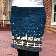 a woman is standing on the sidewalk wearing a knitted skirt with sheep and snowflakes