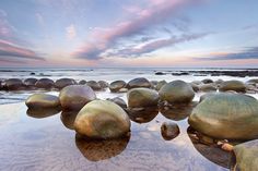 some rocks and water at the beach with sunset in the backgrounnds