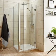 a bathroom with a walk in shower next to a table and chair on the floor